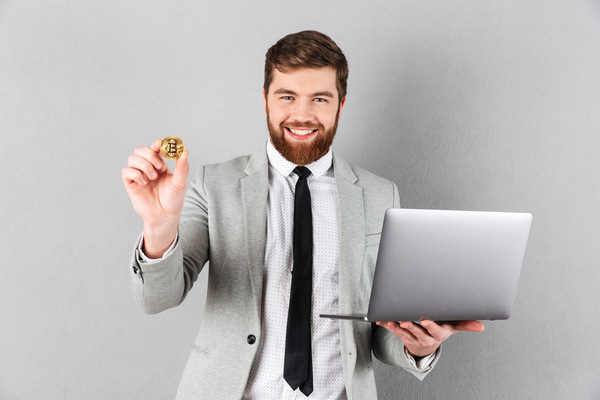 A man satisfied Bitcoin ATM user holding coin and laptop
