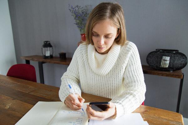 Woman managing money transfer using phone and notebook
