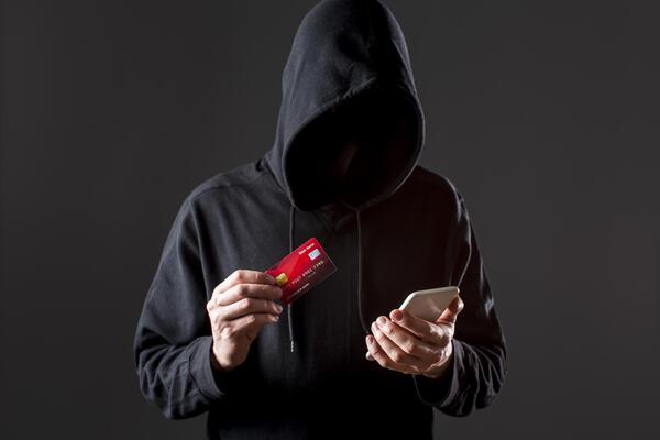 Hacker holding credit card and smartphone secretly
