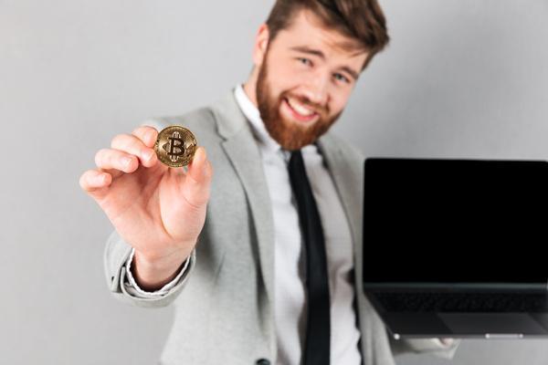 Hombre sonriente que sostiene Bitcoin y una computadora portátil con confianza