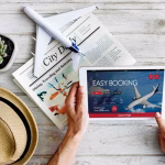 Un hombre reserva un vuelo en una tableta con artículos esenciales de viaje.