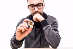 Hombre sosteniendo una moneda Bitcoin mientras considera la seguridad del cajero automático