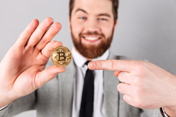 Un hombre sonriente y orgulloso usuario de un cajero automático de Bitcoin sostiene una moneda