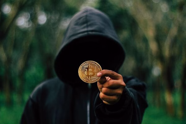Hooded figure holding Bitcoin coin, symbolizing Bitcoin risks.