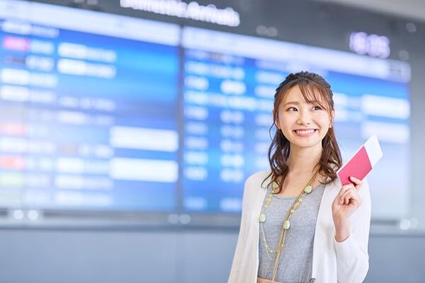 Smiling woman at airport holding her plane tickets confidently.