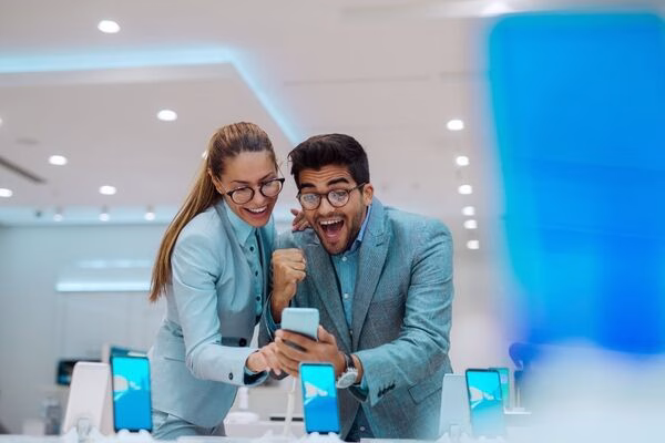 Dos colegas felices verificando el éxito de los pagos transfronterizos por teléfono.

