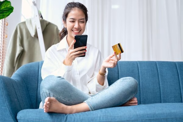 Mujer que usa un teléfono y una tarjeta para pagos transfronterizos en casa
