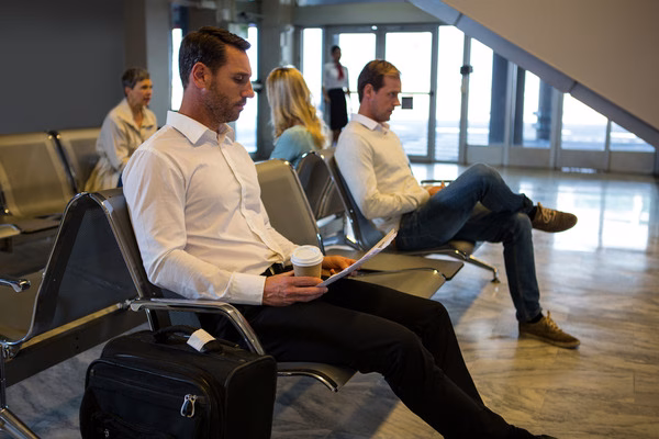 Man sitting in airport lounge with coffee and plane tickets.

