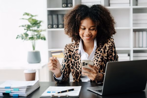 Mujer que usa un teléfono y una tarjeta para realizar pagos transfronterizos en línea.