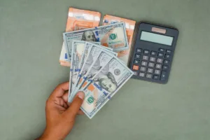 Mano que sostiene dólares estadounidenses con billetes de euro y calculadora
