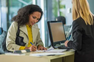 Woman signing documents at bank counter for money transfer.