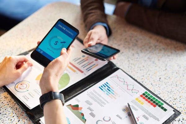 Discusión del equipo de negocios con teléfonos inteligentes y gráficos financieros.
