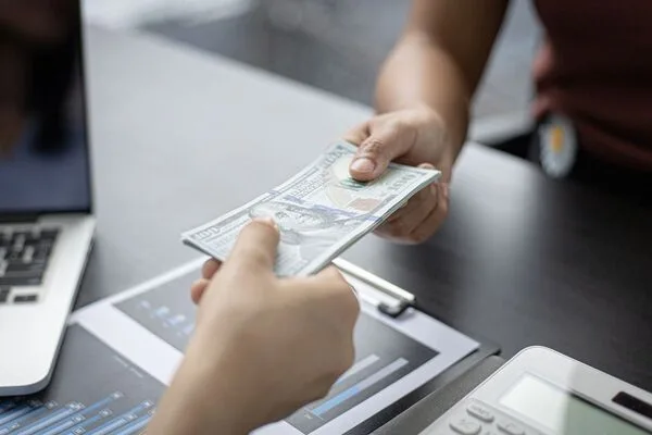 Manos intercambiando dólares en efectivo durante una transferencia de dinero en el escritorio de la oficina.