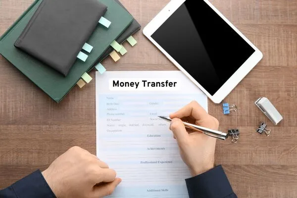 Persona que completa un formulario de transferencia de dinero en un escritorio de madera