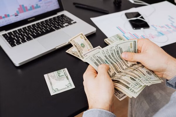 Person counting cash for Cross Border Payments near laptop.