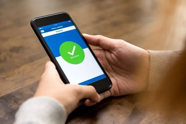 Manos sosteniendo el teléfono mostrando que la transferencia de dinero se completó exitosamente.
