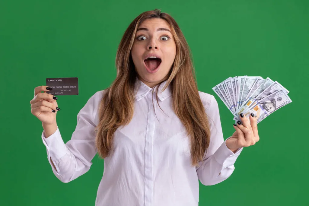 Mujer sorprendida sosteniendo una tarjeta de crédito y dinero en efectivo