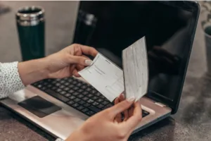Woman holding paycheck in front of laptop for Check Cashing.