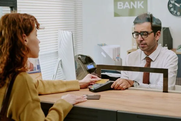 Man behind glass at counter helping woman cash a check.