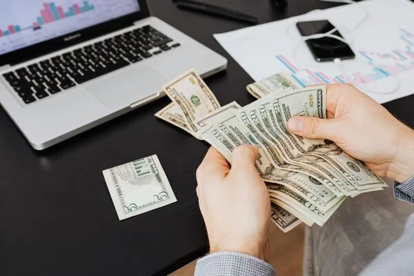 Persona contando billetes de dólar después de una transferencia de dinero en línea exitosa.