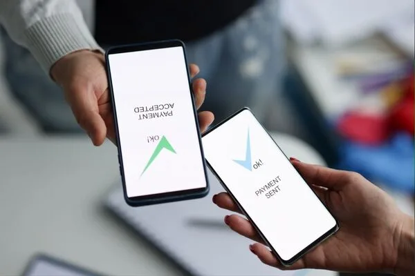Dos teléfonos inteligentes que confirman el envío de dinero con pantalla de pago aceptado.
