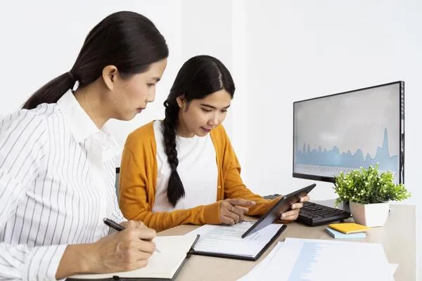 Two women analyzing digital reports for financial efficiency
