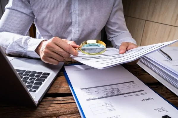 Businessman using magnifying glass to detect Check Cashing fraud.
