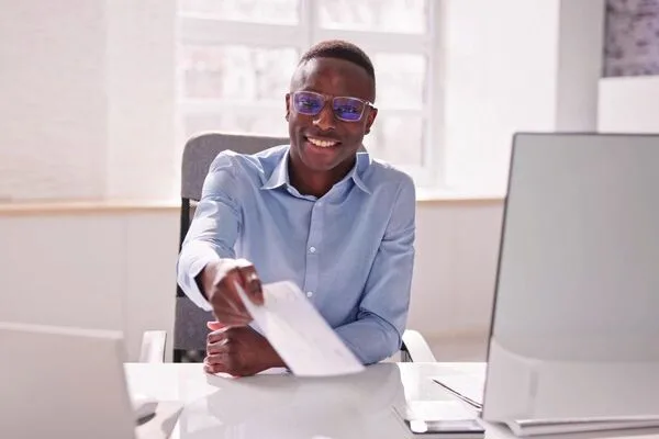 Empleado sonriendo y extendiendo un cheque para que el cliente lo cobre.