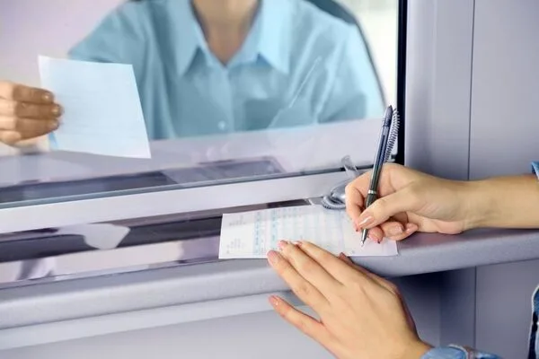 Cajero ayuda a un cliente a cobrar un cheque a través de una ventana de vidrio segura.