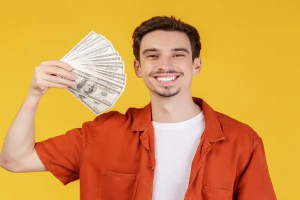 Hombre sonriente que sostiene efectivo después de cobrar un cheque con éxito
