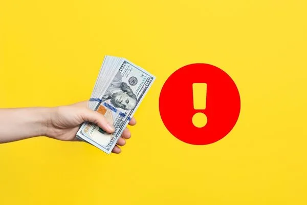 Mano sosteniendo dinero con señal de advertencia de cobro de cheques