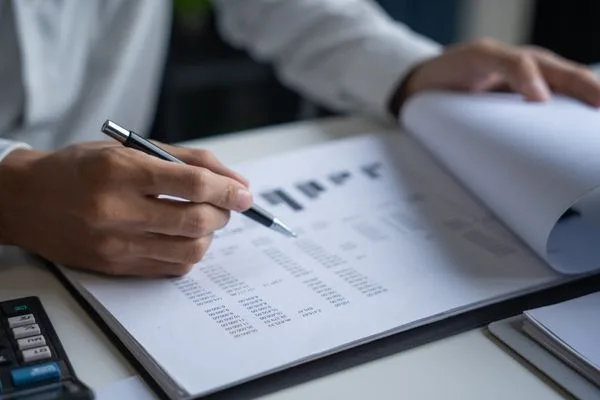 Hand holding pen while analyzing Money Order transaction records.
