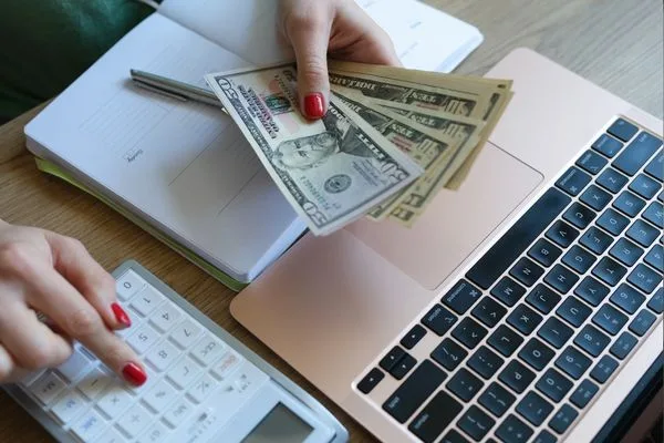 Mujer calcula pagos de giros postales con efectivo y una computadora portátil.
