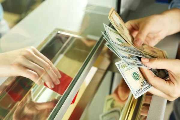 Cliente intercambiando efectivo en ventanilla durante una transacción de cobro de cheques