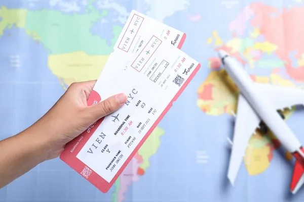 Mano sosteniendo billetes de avión sobre un fondo de mapa mundial