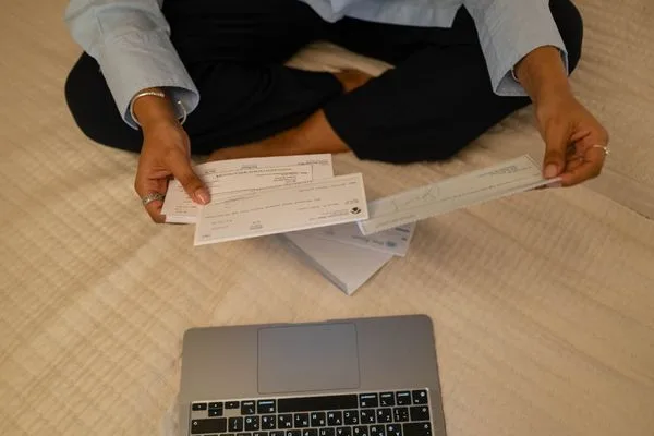 Persona que sostiene cheques con una computadora portátil para el proceso de cobro de cheques