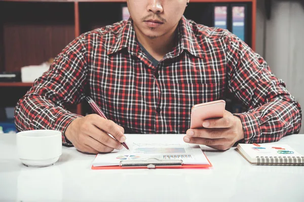 Hombre llenando un formulario de orden de pago mientras sostiene un teléfono inteligente.