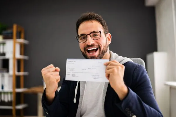 Man with glasses holding Money Order and smiling joyfully.
