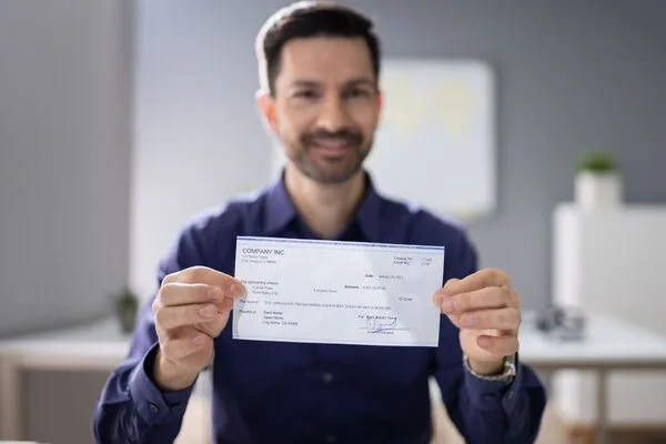Una persona muestra con orgullo su cheque de pago y destaca la conveniente opción de cobro de cheques.