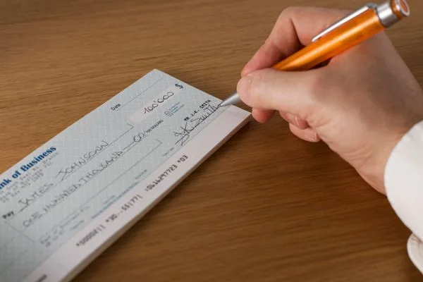 Hand signing a bank check, related to check cashing services.
