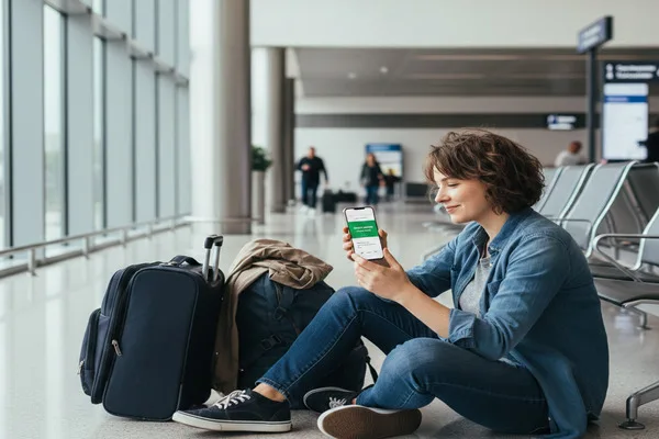 Stranded traveler checking urgent Money Transfer status on smartphone.