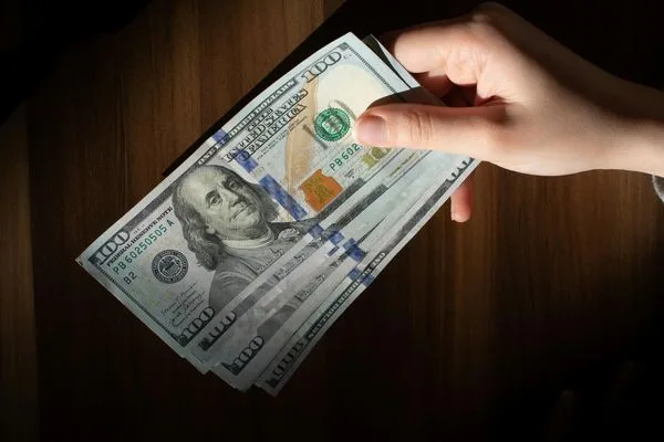 Mano sosteniendo billetes de dólares estadounidenses en una transacción de cambio de divisas