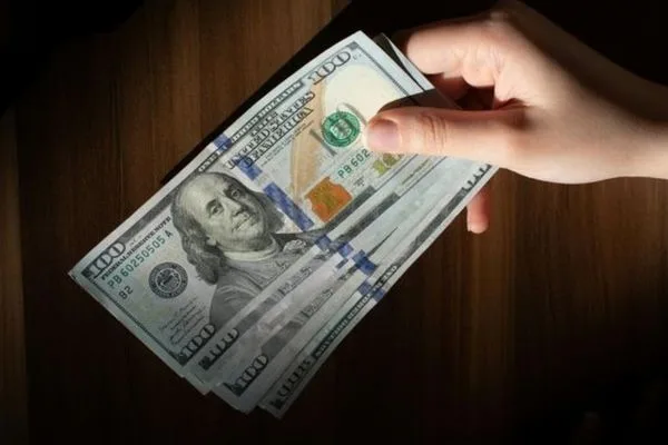Mano sosteniendo billetes de dólares estadounidenses durante el cambio de divisas